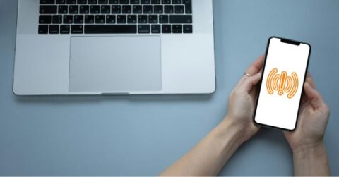 En person holder en smartphone med et orange signalikon ved siden af en bærbar computer.