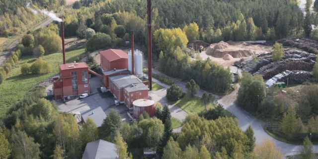 Ilmakuva Paimion Lämpökeskuksen lämpölaitoksesta, jonka ympärillä on metsää, puupolttoainevarastoja ja huoltoteitä. Laitoksen savupiipuista nousee höyryä.